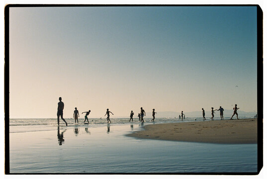 Silhouettes of people walking along beach at sunset