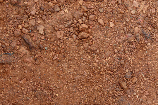 A top-down view of dry, weathered red laterite earth featuring a mix of fine dust, small stones, and rugged pebbles, perfect for industrial or natural backgrounds.