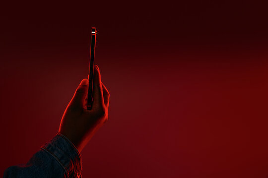Hand Holding Smartphone Against Red Neon Gradient Background