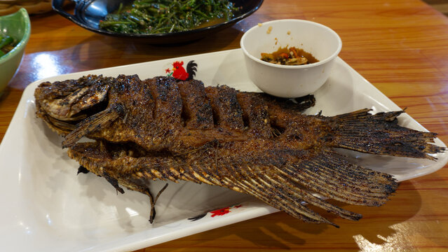 Gurame bakar madu  (Honey-Grilled Gurame Fish) : Grilled gourami fish with honey and soy sauce. Served with chili sauce on a white plate.