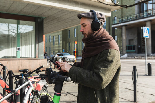 Man using smartphone to unlock electric scooter in the city.
