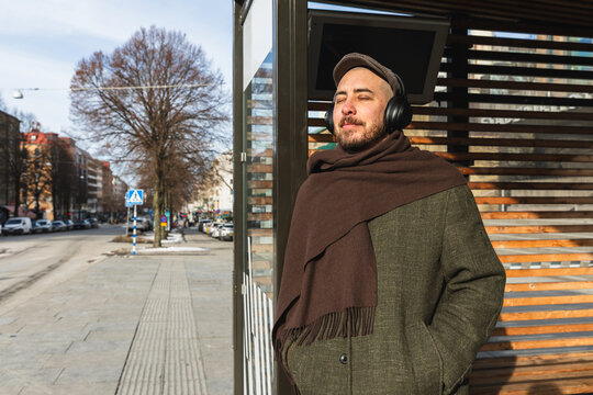 Man with eyes closed listening to music at a city bus stop