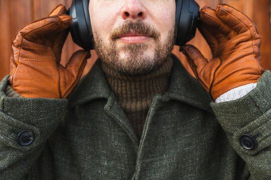 Close up of bearded man wearing olive green wool coat and headphones.