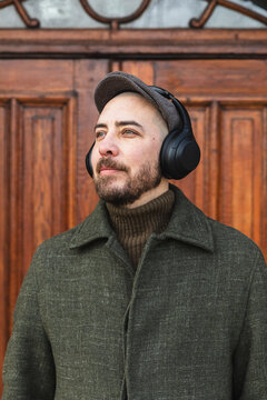 Thoughtful man in winter coat and headphones looking away outdoors.