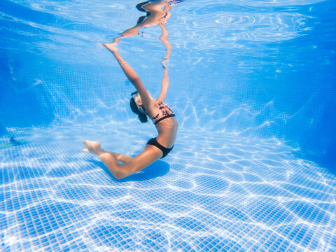 Girl doing acrobatic exercises and synchronized swimming in a pool. 
