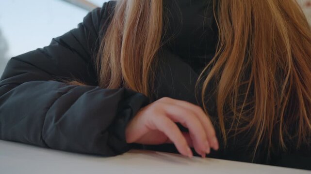 Caucasian woman at cafe counter, poised hand on tabletop, winter jacket with hood, long red hair, neutral expression, subtle furtive motion suggesting snatcher, ambient daylight through window,
