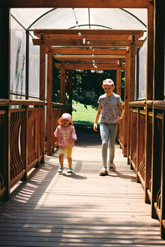 Two happy siblings cross a wooden bridge over a river.
