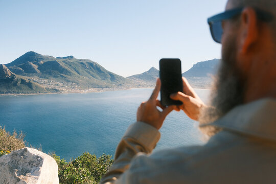 Bearded man taking photo of coastal landscape in Cape Town
