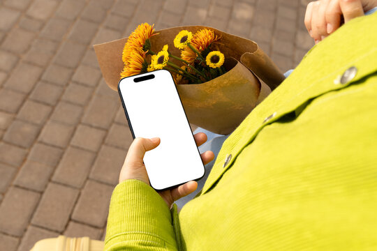 Person holding a phone and a bouquet of flowers in a lively setting