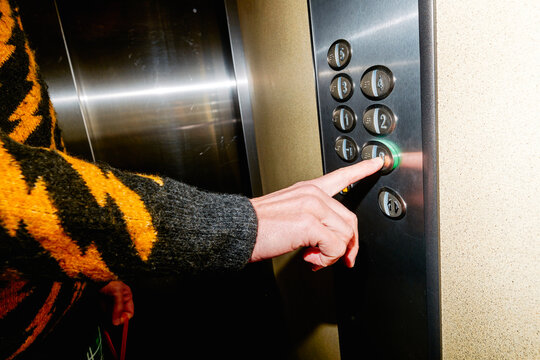 a man in a patterned sweater presses the 0 button inside an elevator