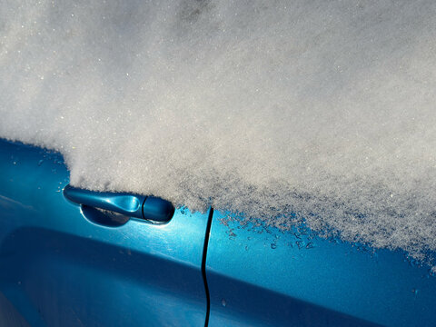 Snow covers a blue car parked outside in winter