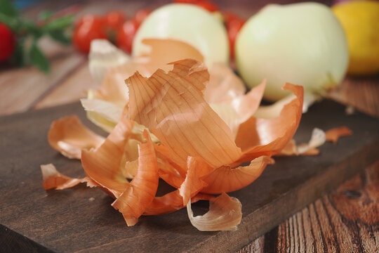 Onion peels and whole onions on wooden cutting board