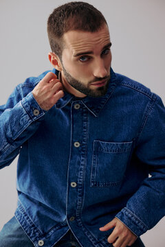 Man Adjusts Collar in Denim Jacket Against Simple Backdrop
