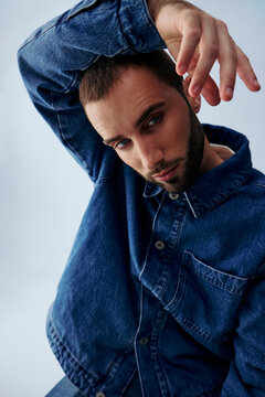 Man in Denim Shirt Poses With Arm Raised in Simple Studio Setting