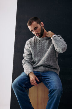 Man Sits on a Cube Wearing Gray Sweater and Blue Jeans