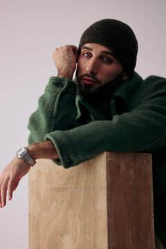 Man Poses Against a Wooden Box While Wearing a Beanie and Coat