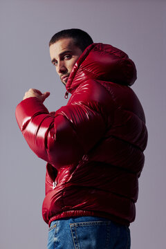 Man Poses in a Red Puffer Jacket Against a Simple Background