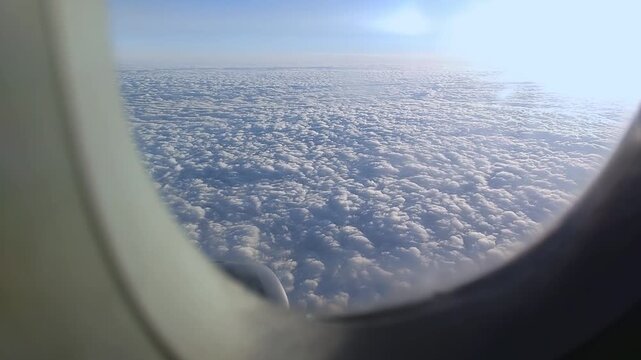Airplane window view showcasing a vast expanse of fluffy white clouds under a clear blue sky, with a glimpse of the aircraft wing visible in the lower corner