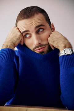 Man Sits With Hands on His Face in a Blue Sweater Indoors