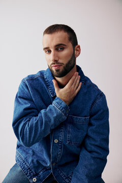 Man Poses in Blue Denim Jacket With Hand on Neck in Studio Setting
