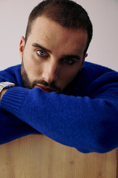 Man in Blue Sweater Resting His Arms on Wooden Surface Indoors