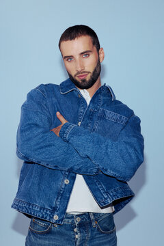 Man Poses Confidently in Denim Jacket Against a Light Blue Background
