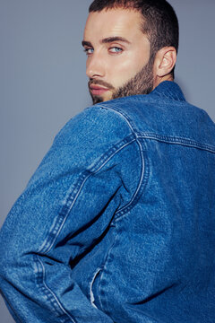 Man in Denim Jacket Poses Against Plain Background