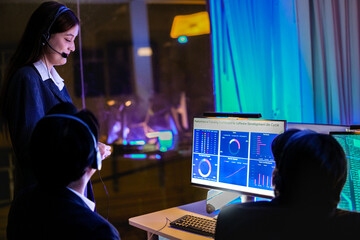 Professional IT support team working in a high-tech command center at night. Focused female...