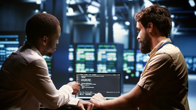 IT developers team writing server script code in data center on laptop terminal. Teamworking programmers doing maintenance work in high tech facility updating rigs software