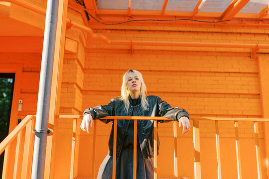 Woman in Black Jacket Stands on Orange Balcony in Sunny Weather