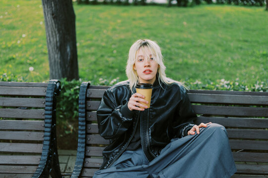 Young Person Sits on Park Bench With Coffee in Hand