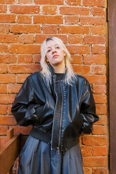 Young Person Stands Near Brick Wall Wearing Black Jacket