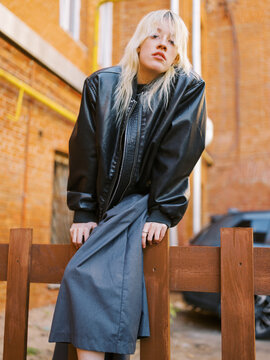 Model Poses on Wooden Fence in Urban Setting During Daylight