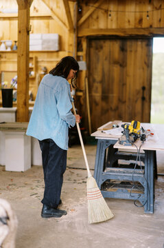 woman in barn sweeping the concrete floor with broom
