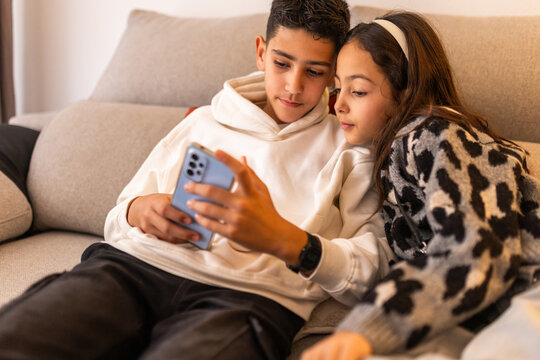 Siblings sitting on sofa looking at mobile phone together
