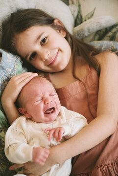 Older Sister Holding Crying Newborn Baby at Home
