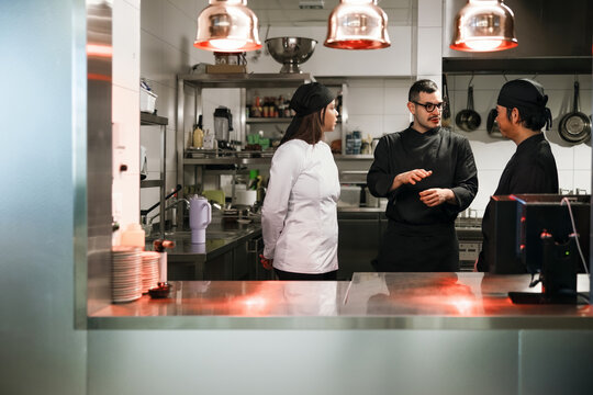 Three Chefs Discussing Orders in Professional Kitchen