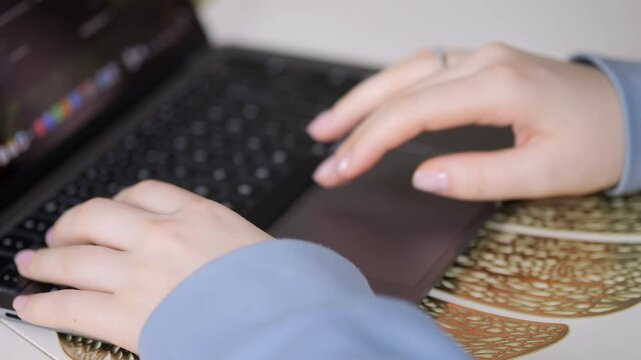 Hands type on laptop keyboard. Fingers press keys with precision. Ring glints on right hand. Mouse pad beneath palm. Soft lighting highlights skin texture. Background slightly blurred for focus