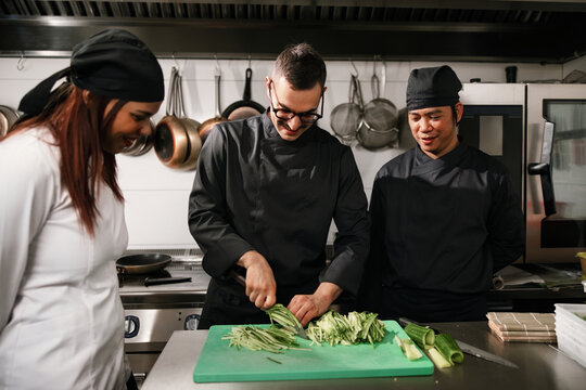 Chefs Working Together In Commercial Kitchen Preparing Vegetables
