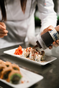 Chef Adding Sauce to Sushi Rolls in Restaurant Kitchen