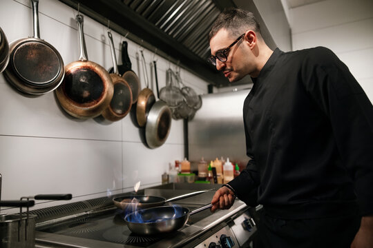Professional Chef Cooking With Flaming Pan In Kitchen