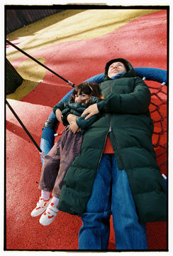 Mother and daughter relaxing together on playground swing