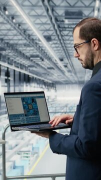 Vertical video Reviewing schematics, laptop and engineer man in semiconductors smart factory. Overseeing integrated circuits infrastructure layouts, EDA software and manager in industry 4.0 plant