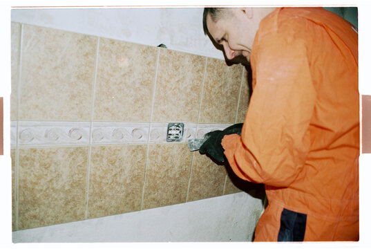 Worker in Orange Coveralls Removing Wall Tiles During Renovation