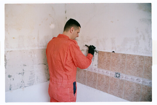Worker in Orange Coveralls Removing Wall Tiles During Renovation