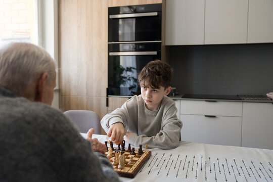 Boy Plays Chess With Senior Man in Modern Kitchen
