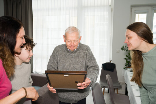Family Members Gather Around Senior Man Looking at a Framed Picture