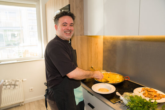 Happy Man Cooking Paella in Kitchen 