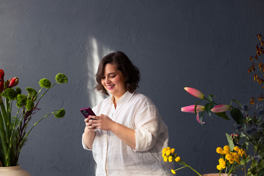 Smiling Woman Using Phone Surrounded by Flowers