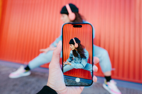 Woman Posing In Front Of Colorful Red Wall Seen Through Phone Screen